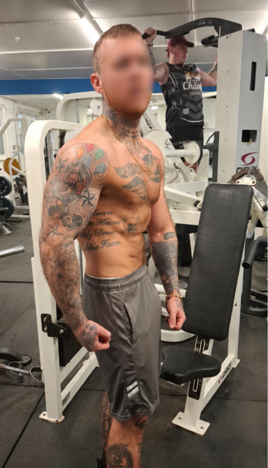 Week 12 Muscular individual with tattoos exercising in a gym setting.